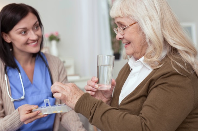 Managing medication. Positive mature woman taking pills from nurse while looking down