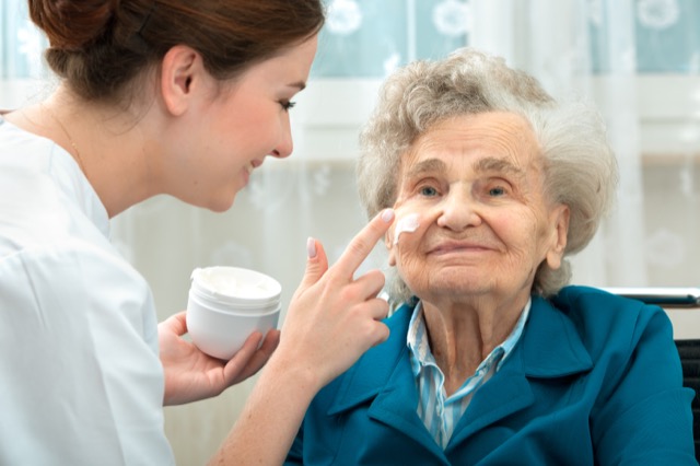 Nurse assists an elderly woman with skin care and hygiene measures at home;
