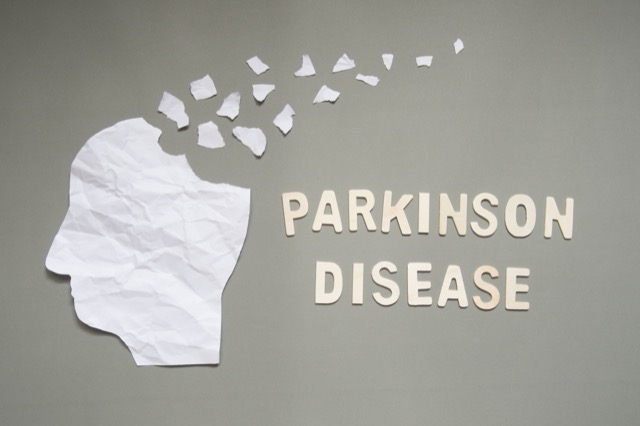 Parkinson's disease concept presented by human head made form white crumpled paper torn on gray background. Creative idea for mental health and neurological disorders