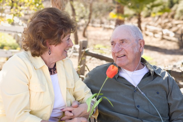 Senior Woman Outside with Seated Man Wearing Oxygen Tubes
