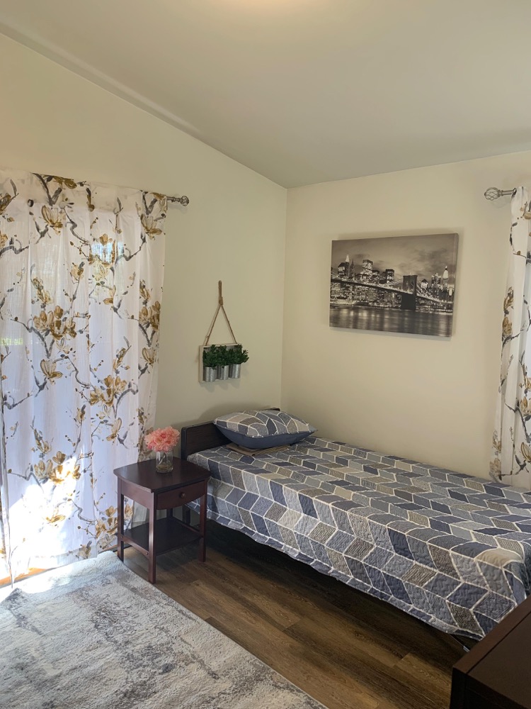 Furnished private bedroom with single bed, nightstand and sunny window